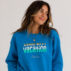 Woman wearing a blue sweatshirt with 'In Desperate Need of a Vacation' text on a plain background