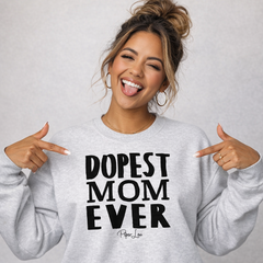 Woman wearing a gray sweatshirt with 'DOPEST MOM EVER' text, pointing at herself.
