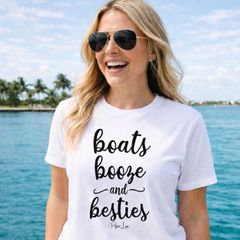 Woman wearing a white t-shirt with 'boats booze and besties' text by the water.