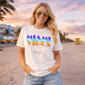Woman wearing a 'Miami Vibes' t-shirt on a beach with palm trees and sunset.